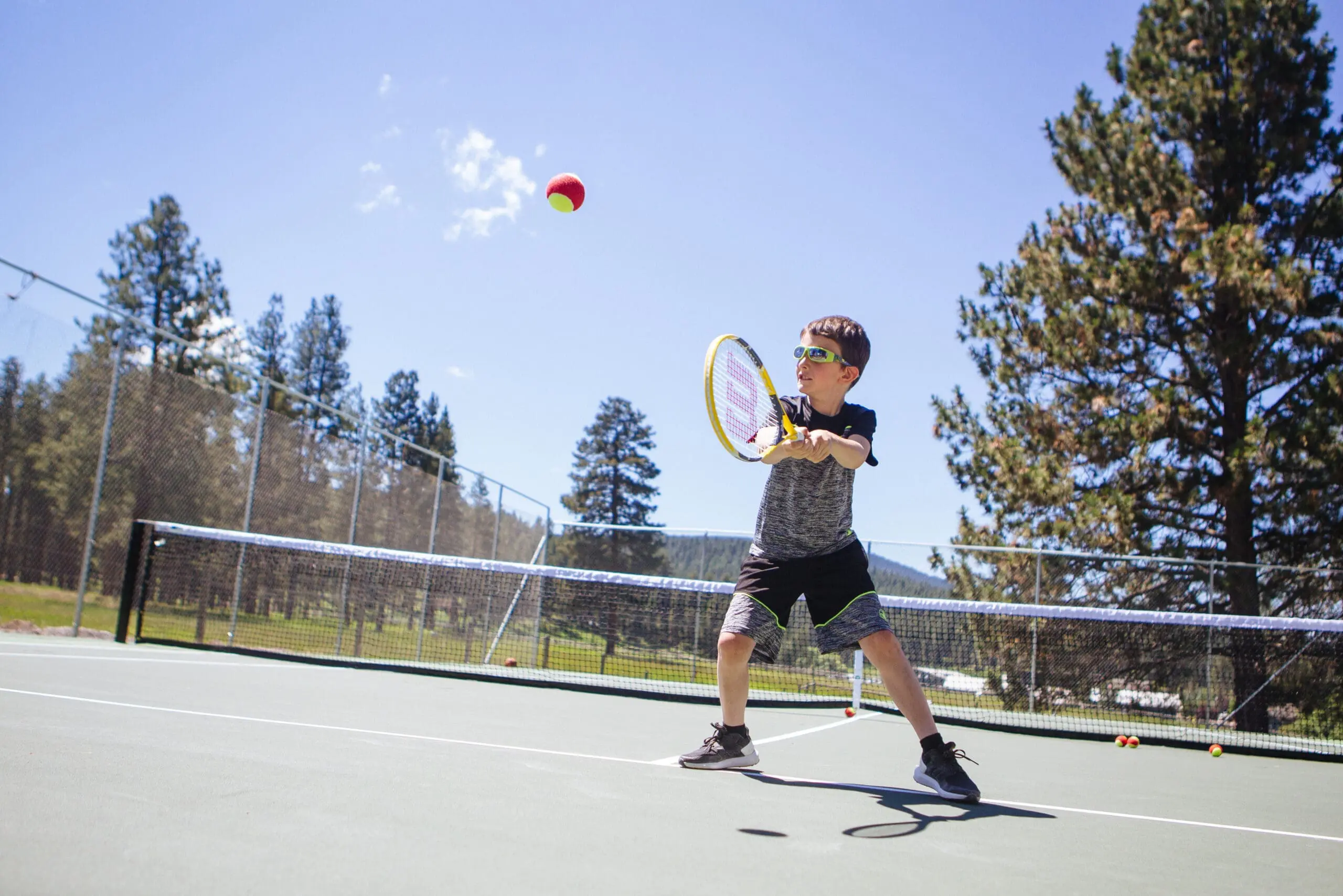 Little boy hitting a tennis ball on a tennis court