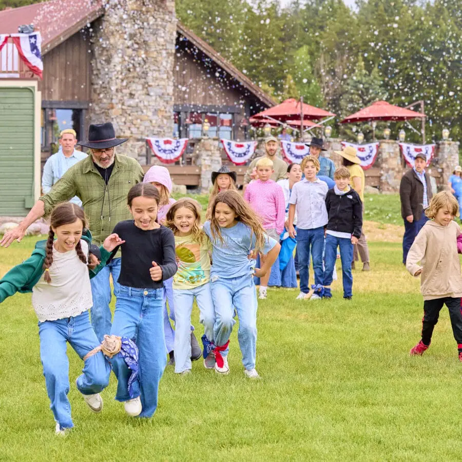 Children playing three-legged race on a grassy hill with fourth of July decorations behind them.