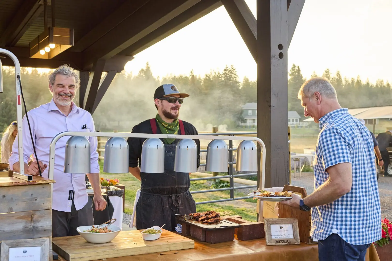Chefs standing under a pavilion outside preparing dishes for guests.