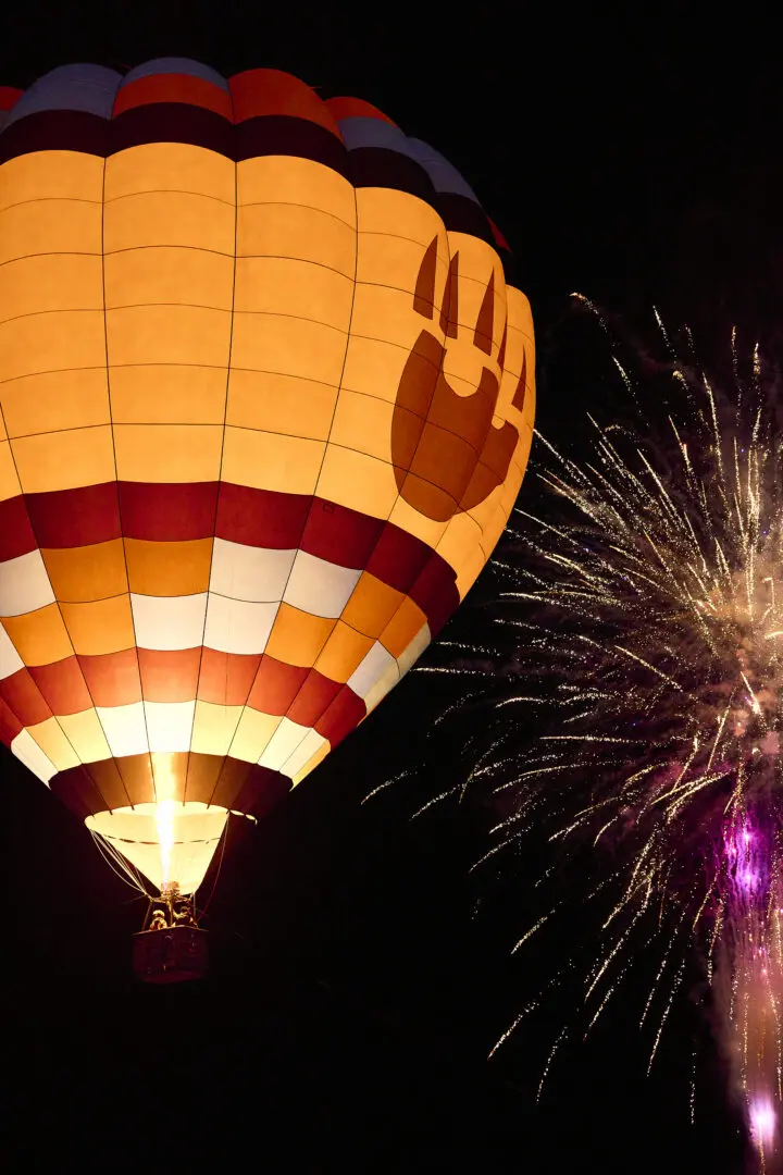 Paws Up hot air balloon in the sky at night with fireworks.