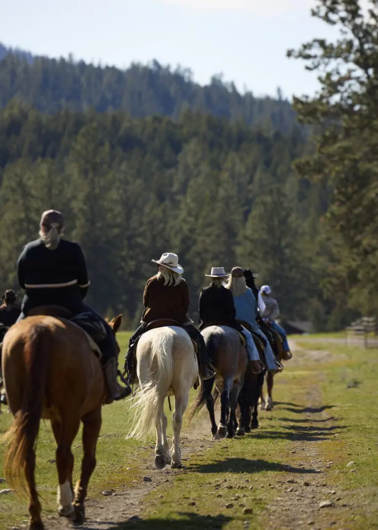 Group of cowgirls riding on a field with mountains in front of them.