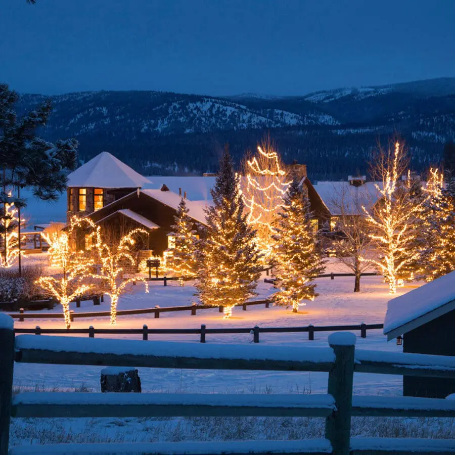 Barn and similar buildings covered in snow at night with white Christmas lights.
