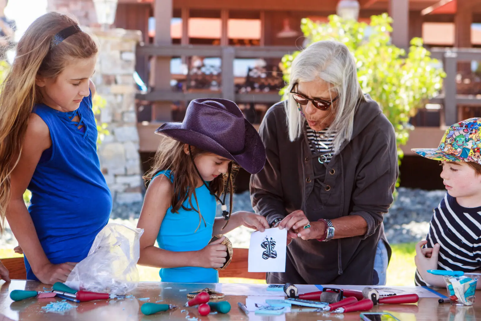 An older woman helping three children make crafts outside.