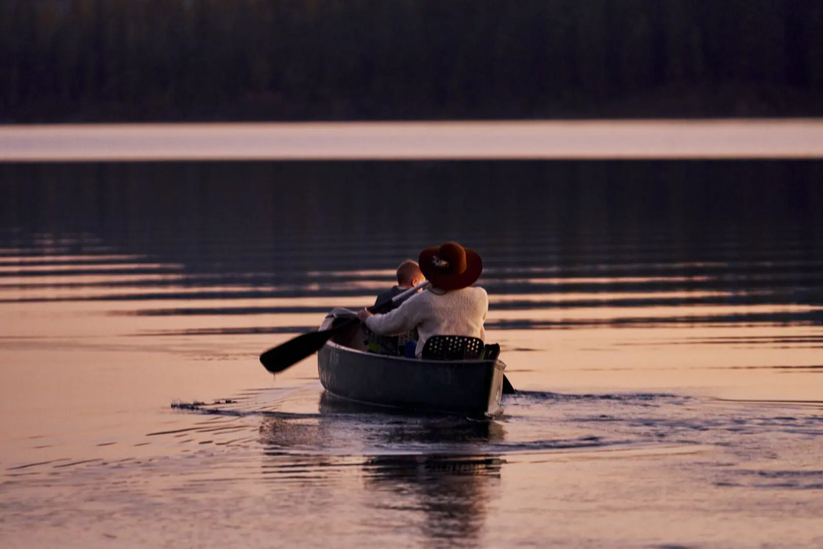 Mother and child paddling in a canoe on water during sunset.