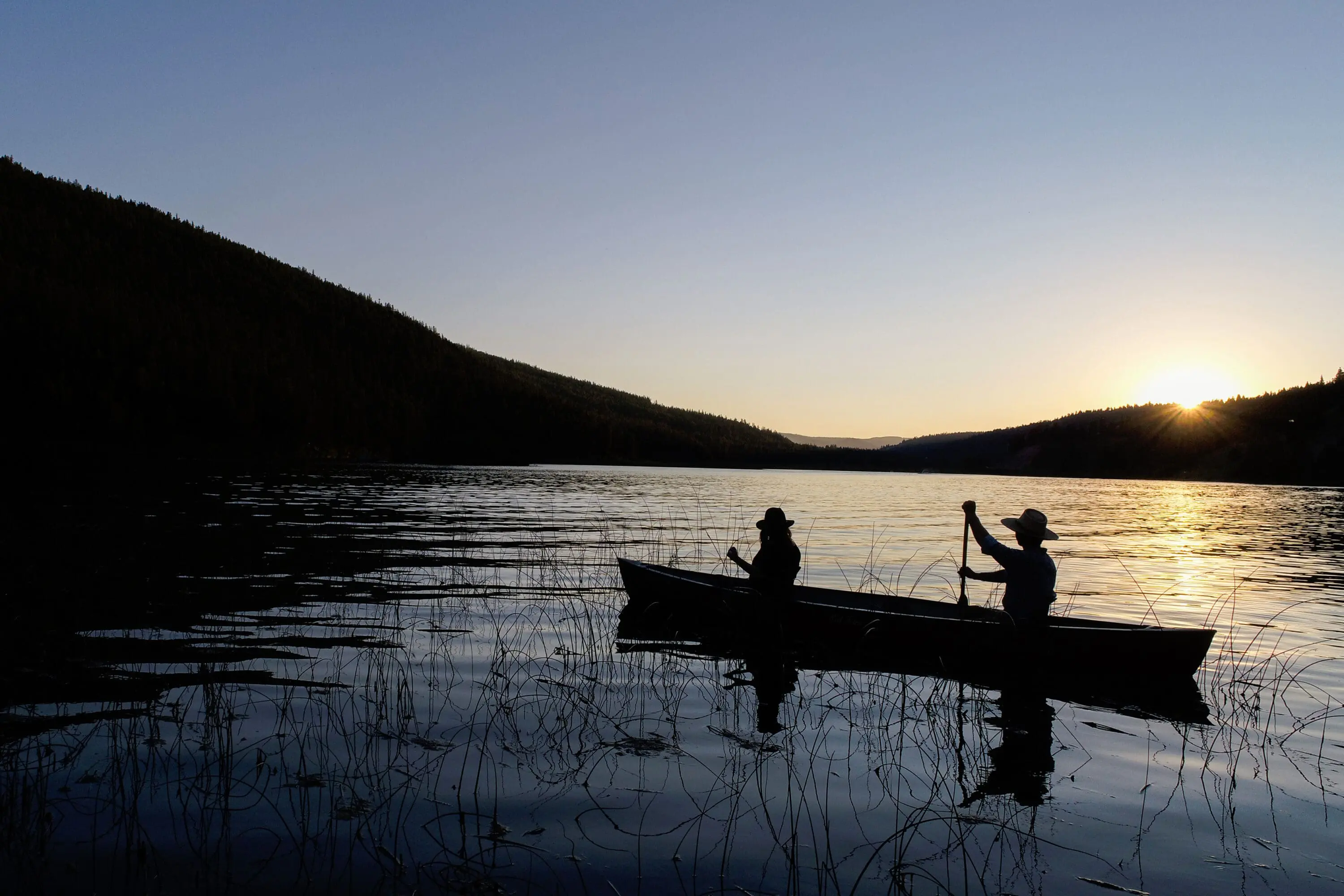 People in the distance paddling in a canoe on water during sunset.