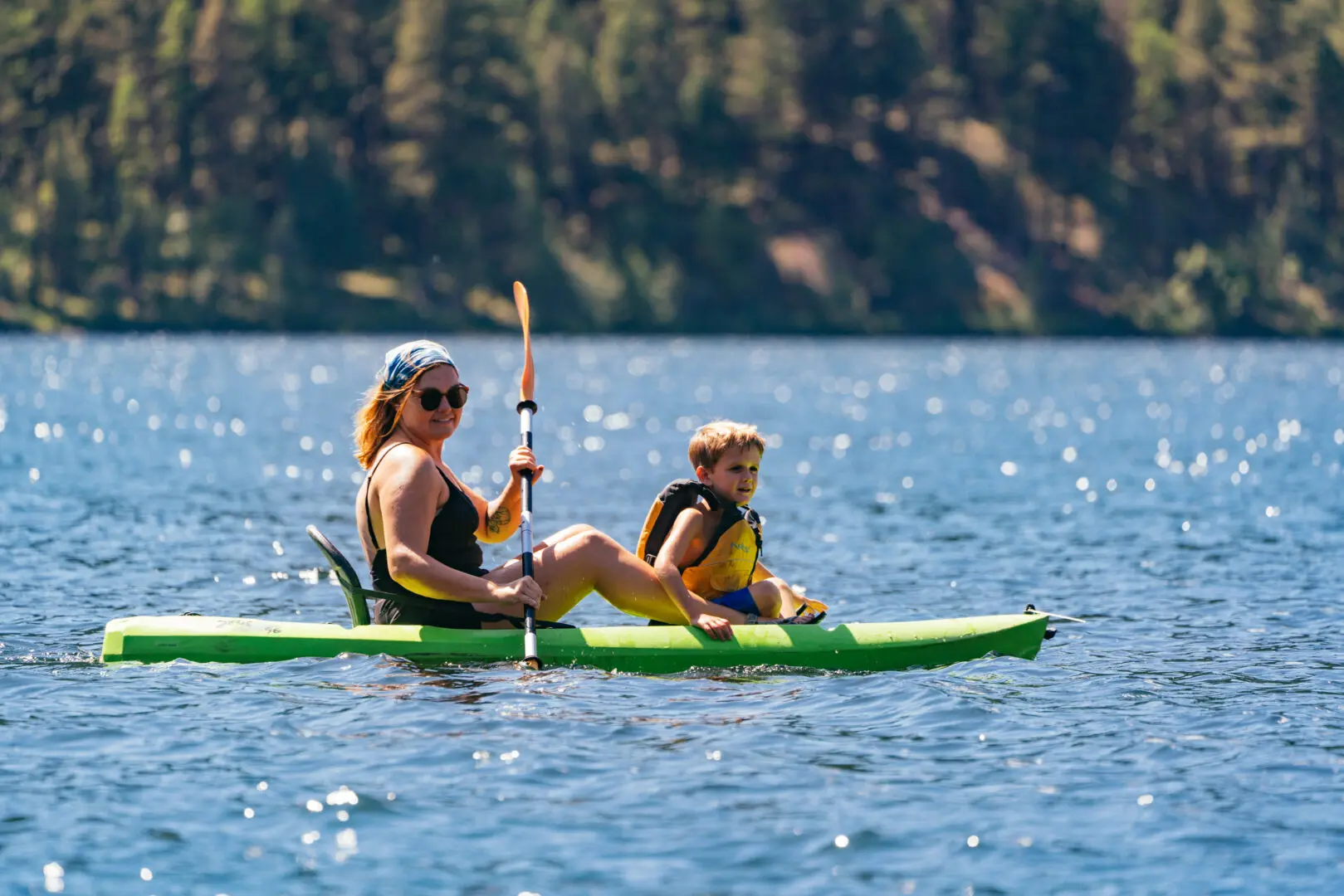Woman and child on a paddle board on a blue lake with trees in the background.