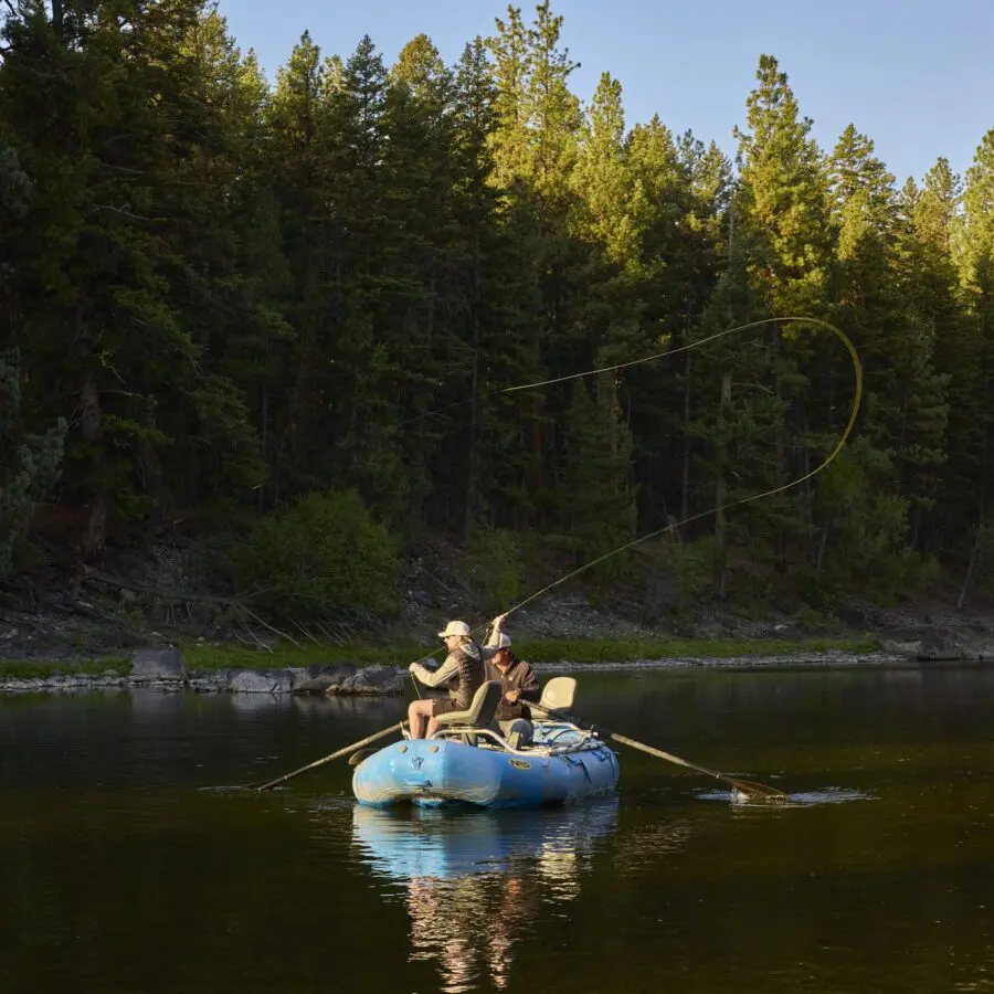 Men fly fishing on a river with trees behind them.