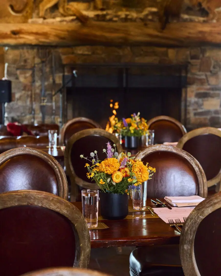 Inside of a dinning area with a stone fireplace and leather chairs.