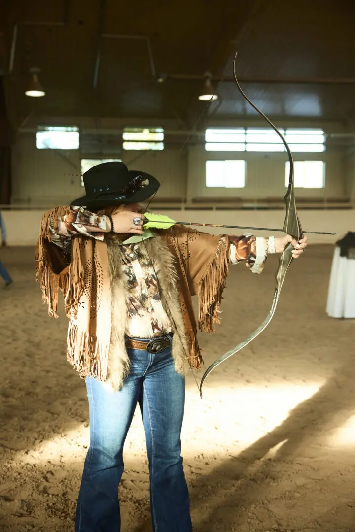 Woman shooting a bow and arrow inside of an arena.