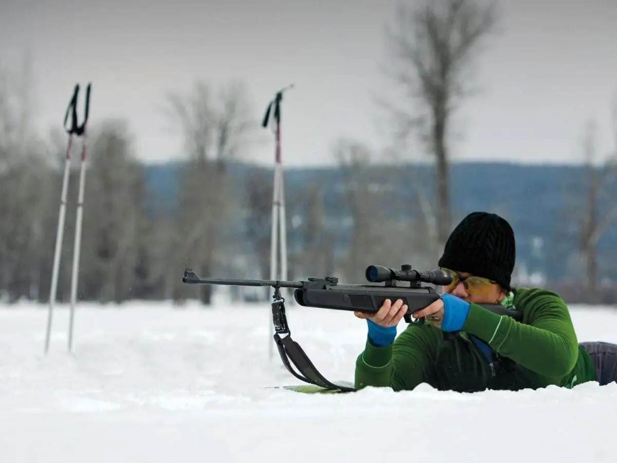 Woman laying in the snow shooting a rifle for biathlon