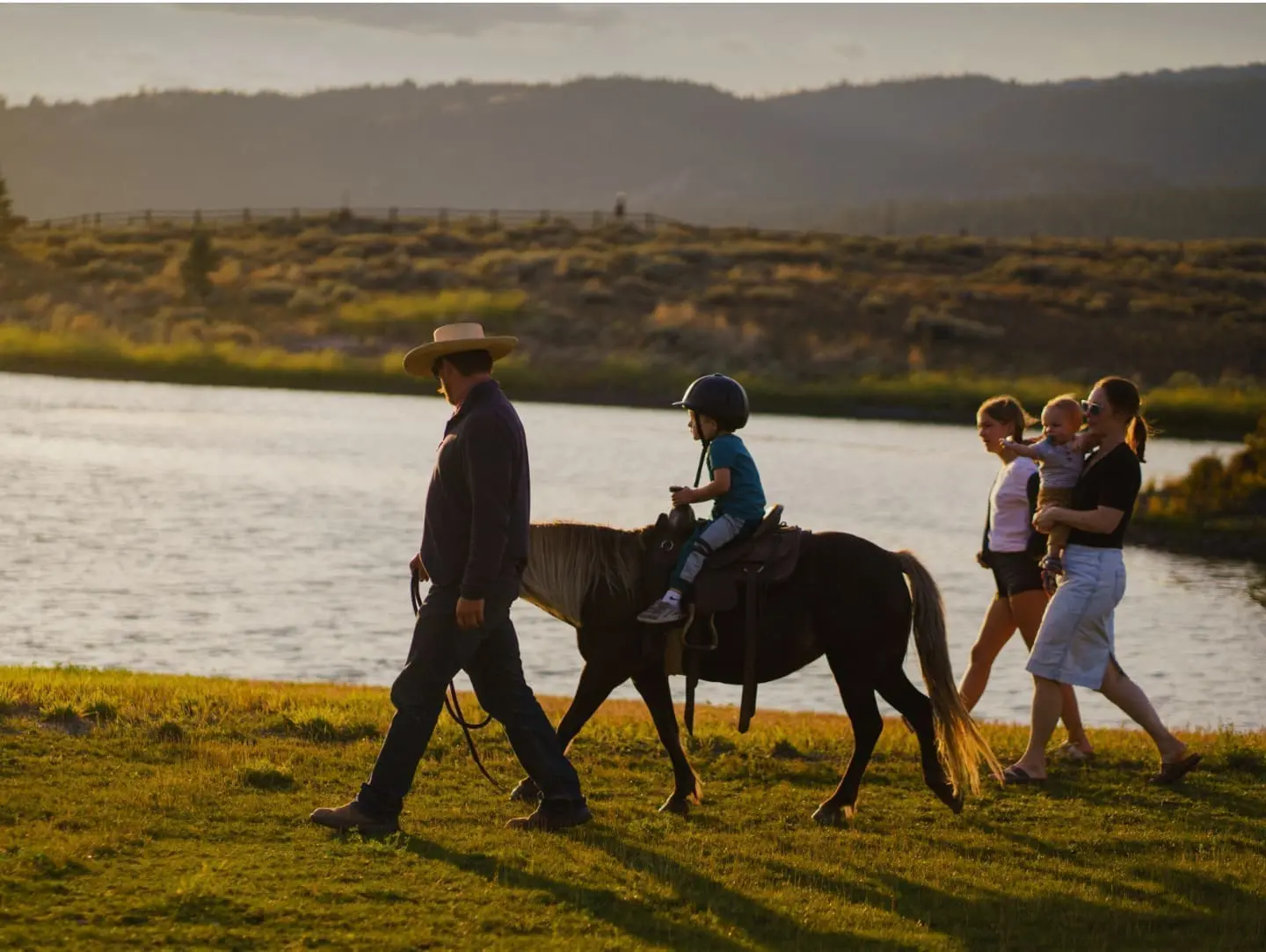 Child riding on a pony being lead by a wrangler beside a mountain river