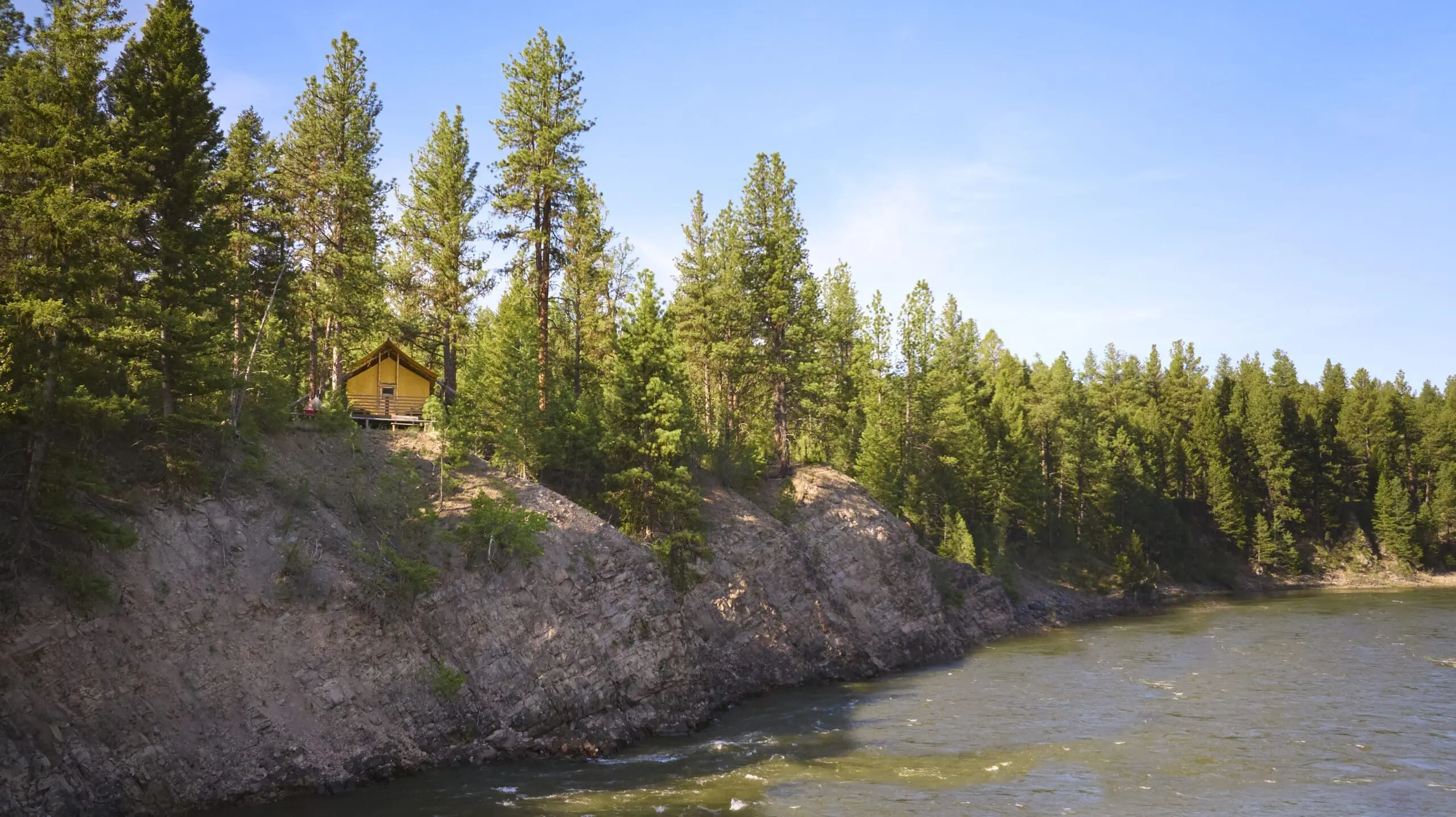 Wide shot of a glamping tent on the top of a cliff beside Blackfoot River
