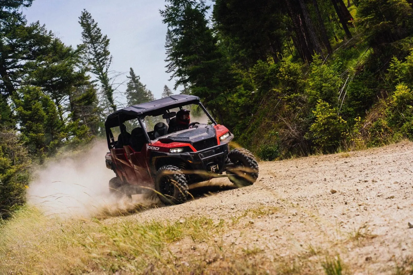 A red Polaris UTV sliding through the dust on a mountain dirt road