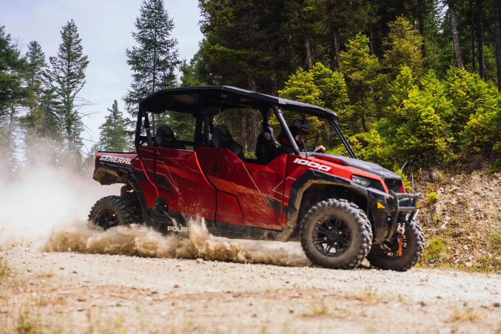 A red Polaris UTV gliding through the dirt on a mountain road