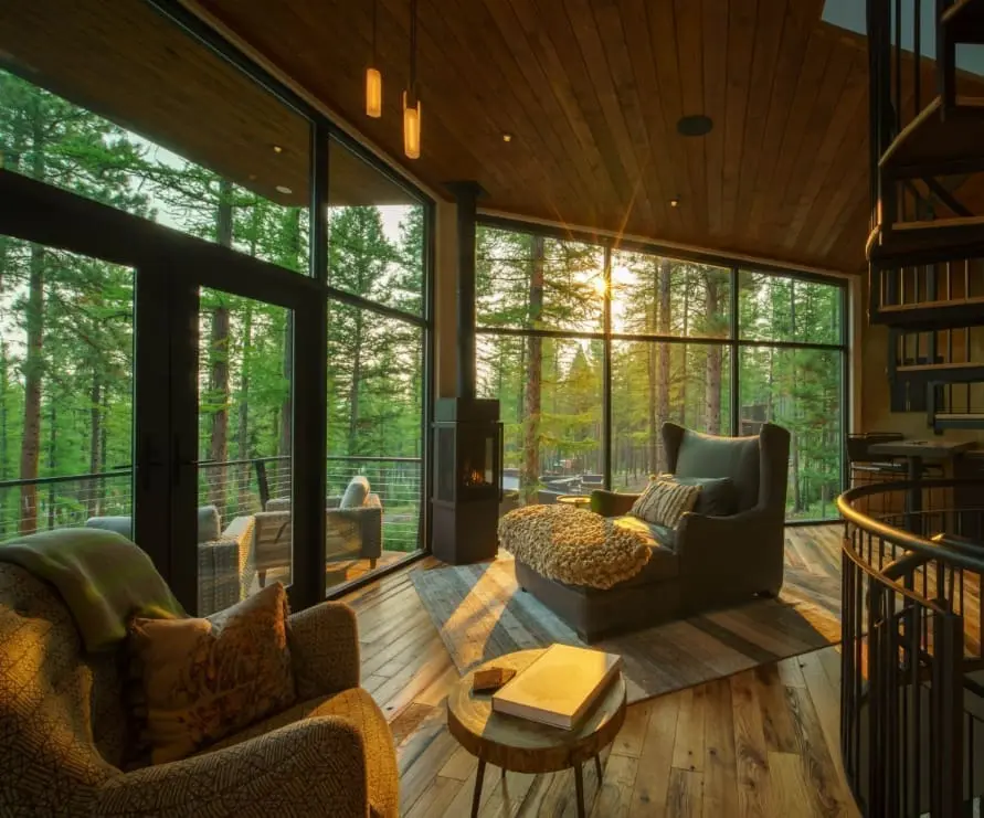 Inside view of the Tree Haus living room at golden hour, showing a leather chair and outdoor deck through the windows