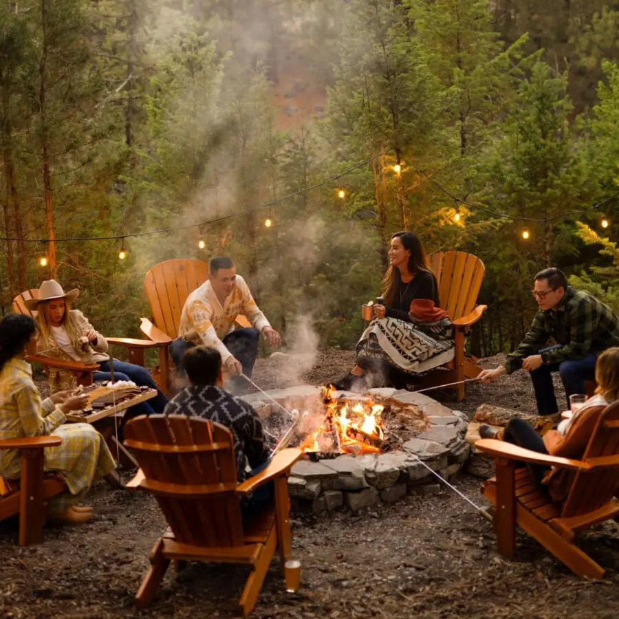 A circle of friends around a campfire roasting smores