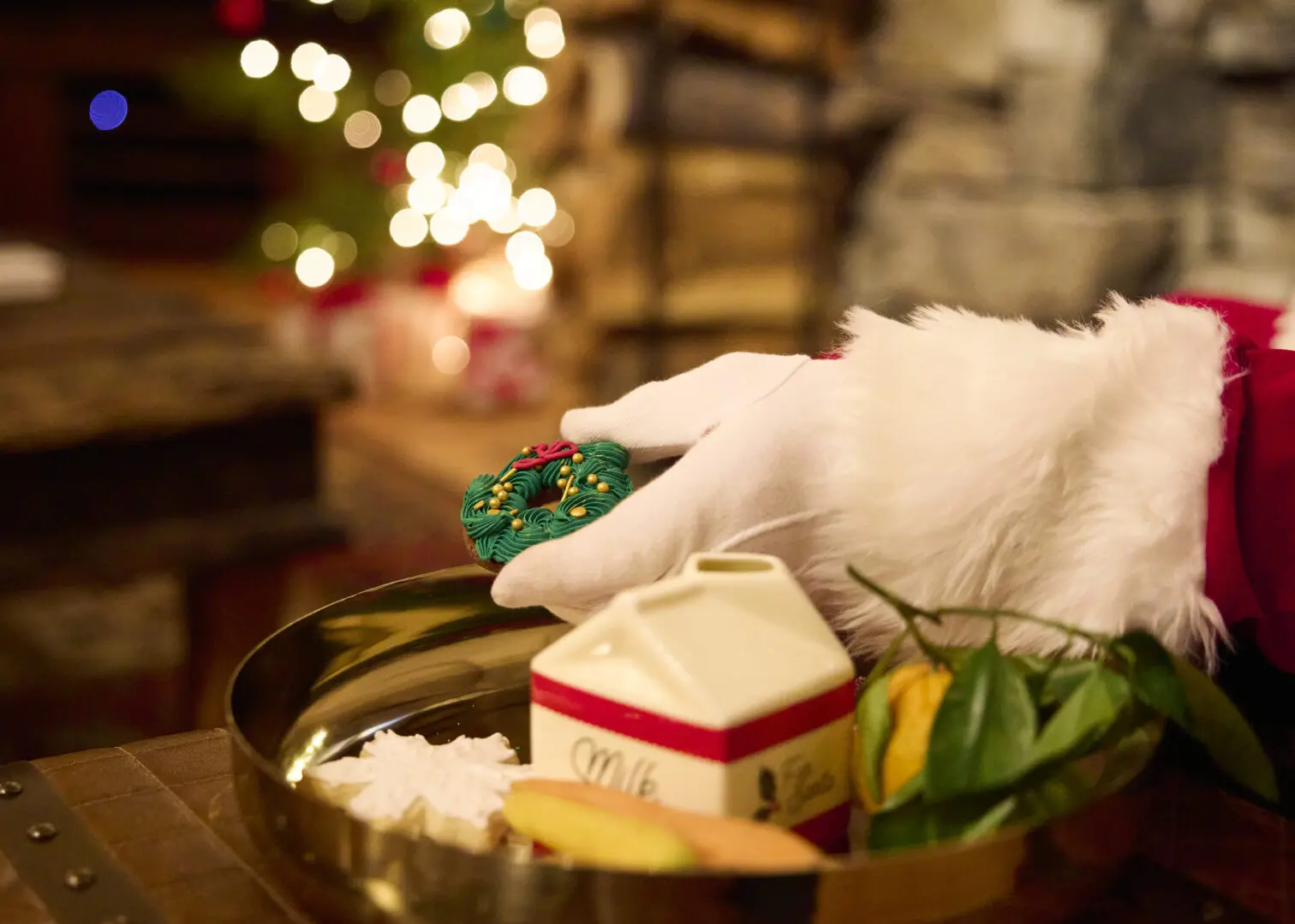 Shot of a gloved "Santa" hand holding a wreath decorated cookie with milk.