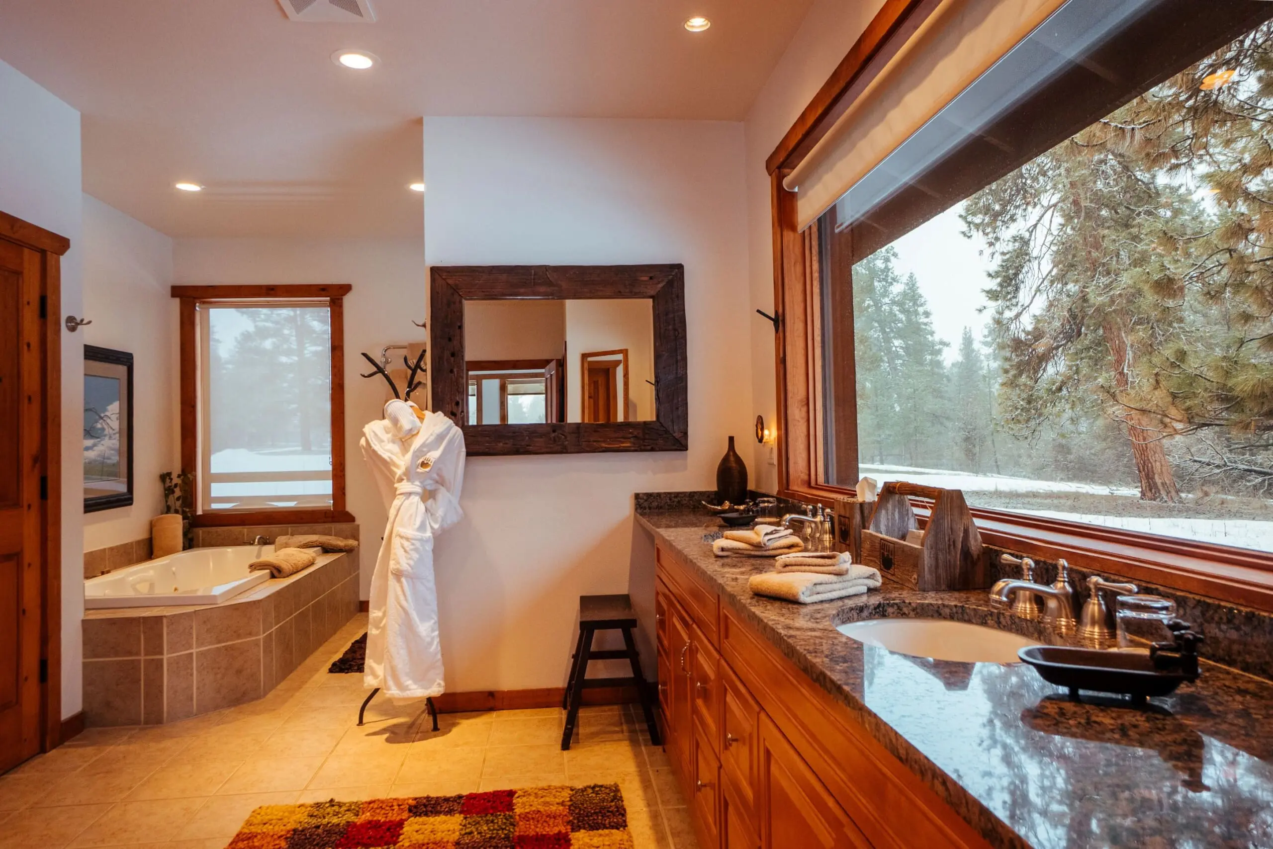 western style luxury bathroom with bathtub, sinks, and window with forest view