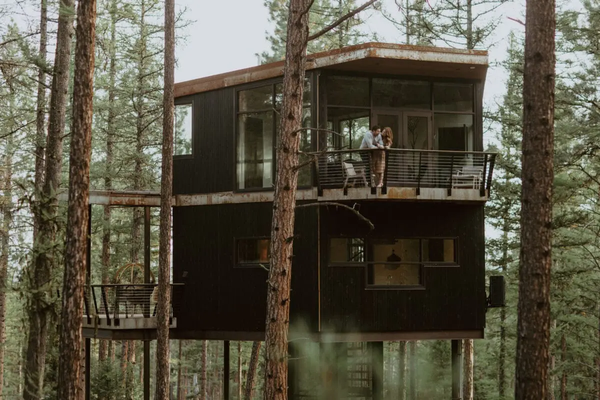 Couple standing at a balcony in a luxury looking treehaus in the woods.