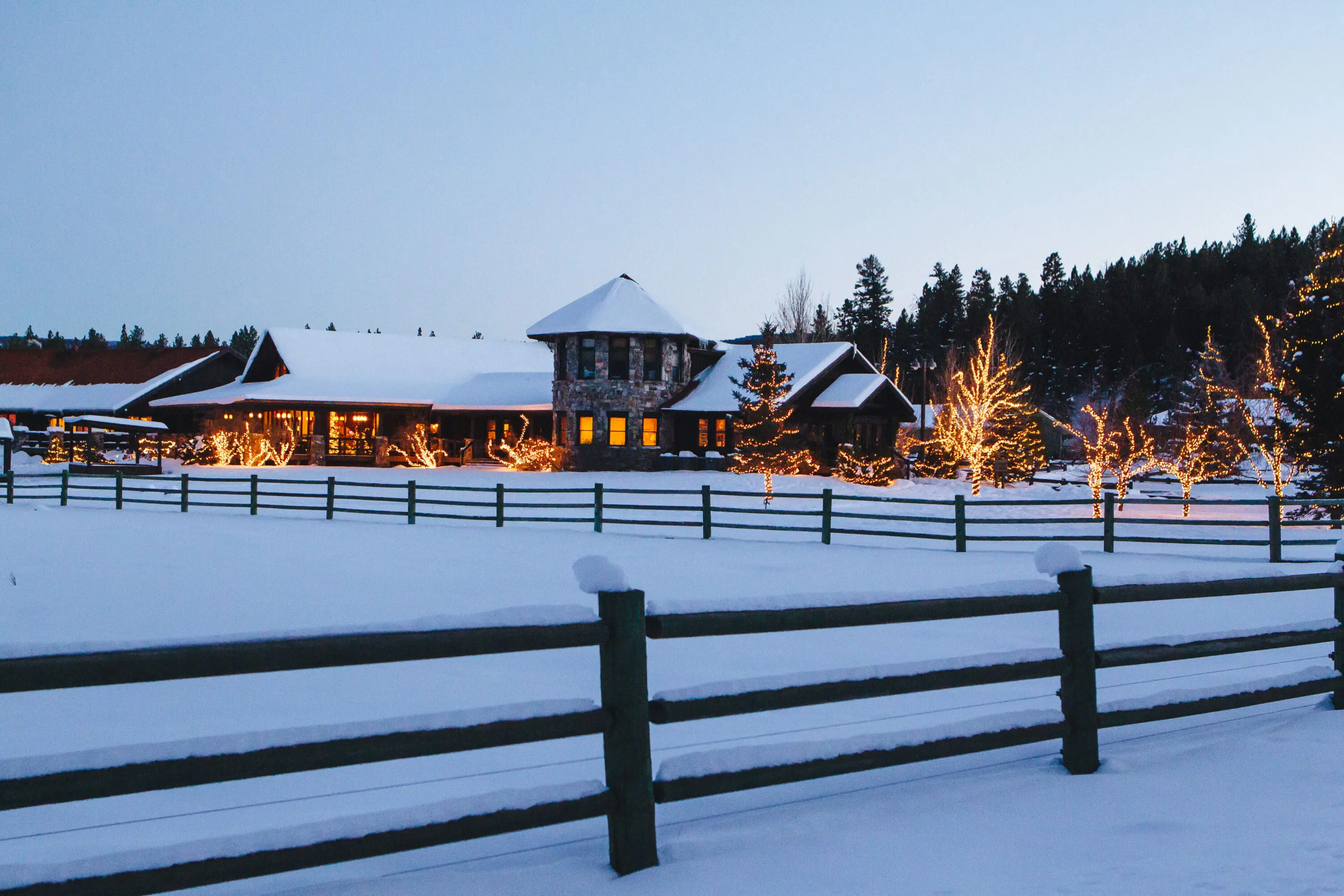 Snow covered building with a wooden fence and fairy lights.