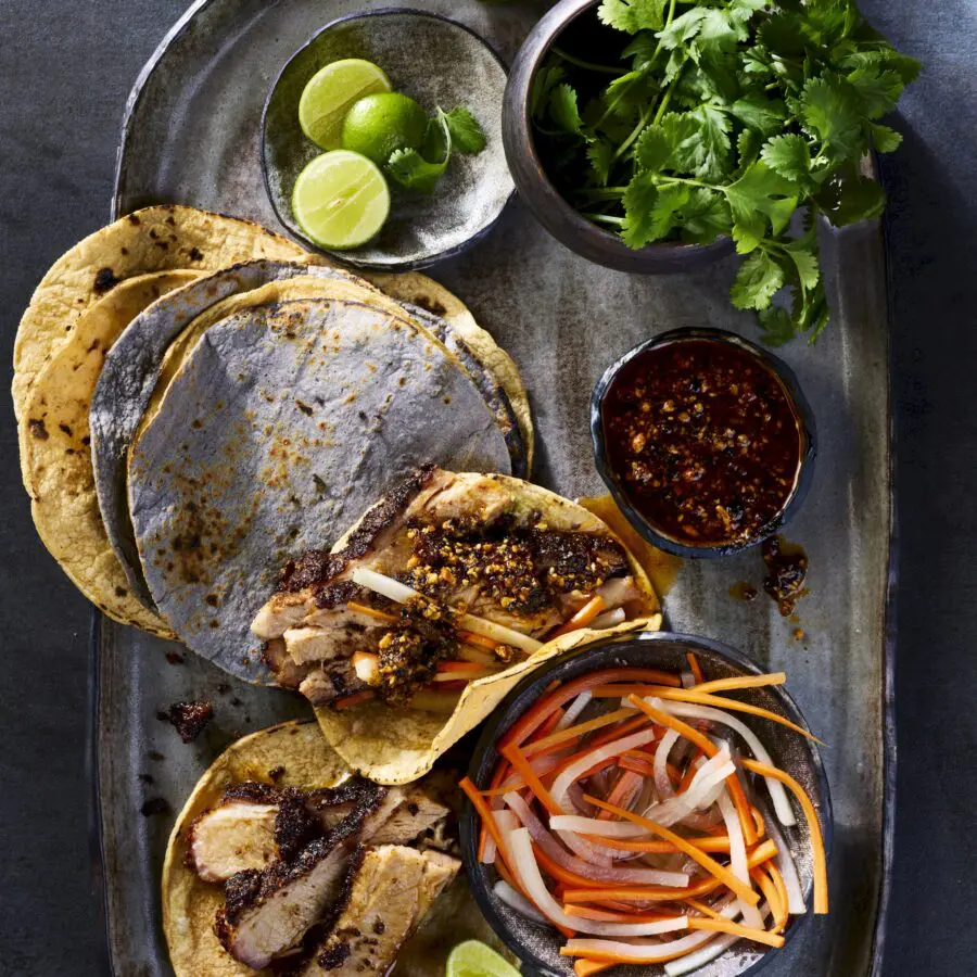 Arranged taco with taco toppings including vegetables, cilantro, limes, and tortillas.