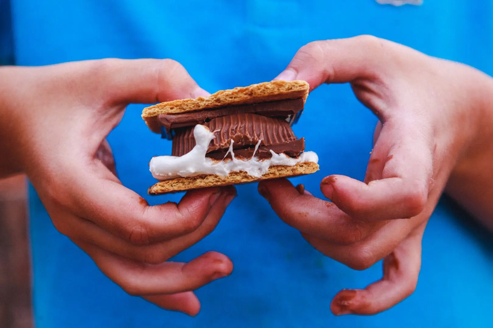 Closeup of a child holding a smores with a Reeces peanut butter cup.