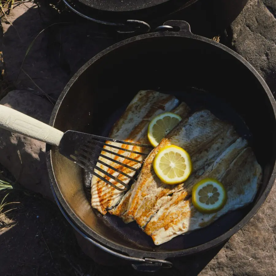 Fish being cooked in a cast iron skillet with lemon slices.