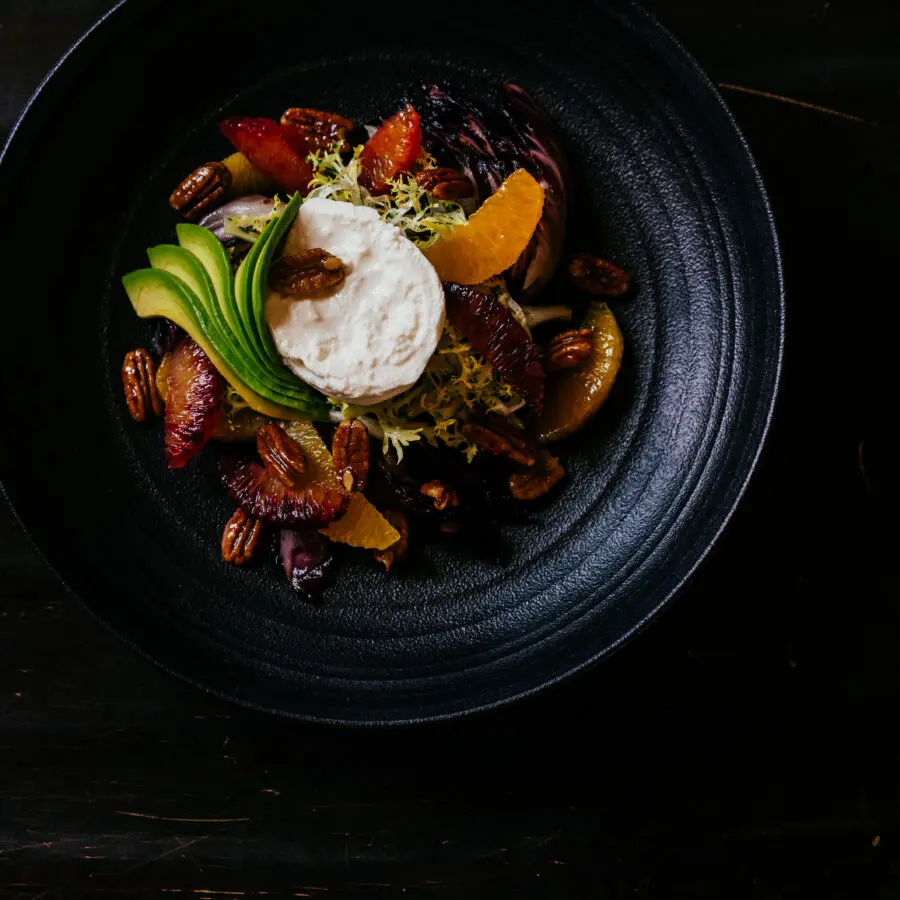 A food dish in a black bowl with avocado, meat, and toppings.
