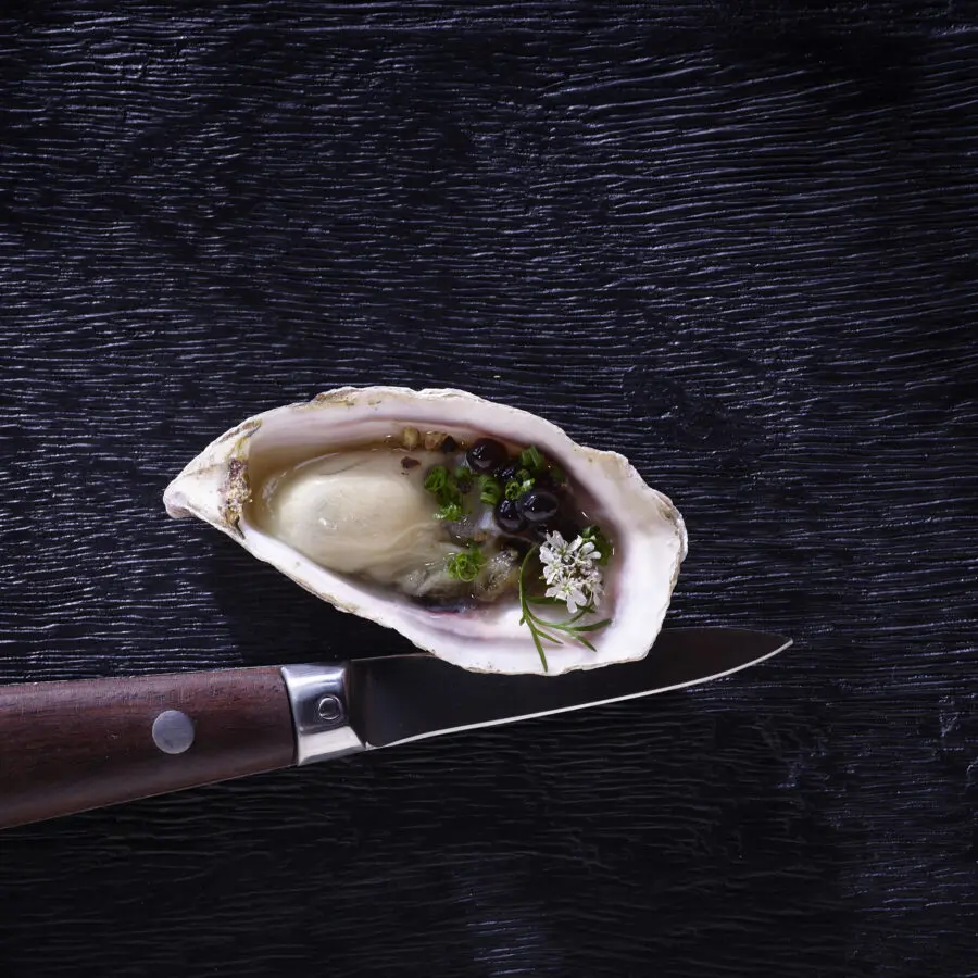 Oyster on a black table with a knife next to it.
