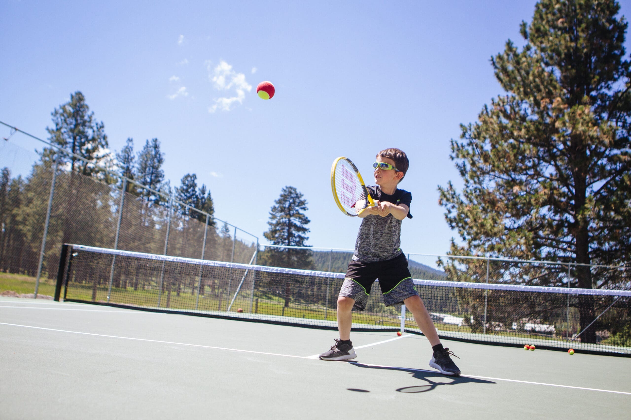 Little boy hitting a tennis ball on a tennis court