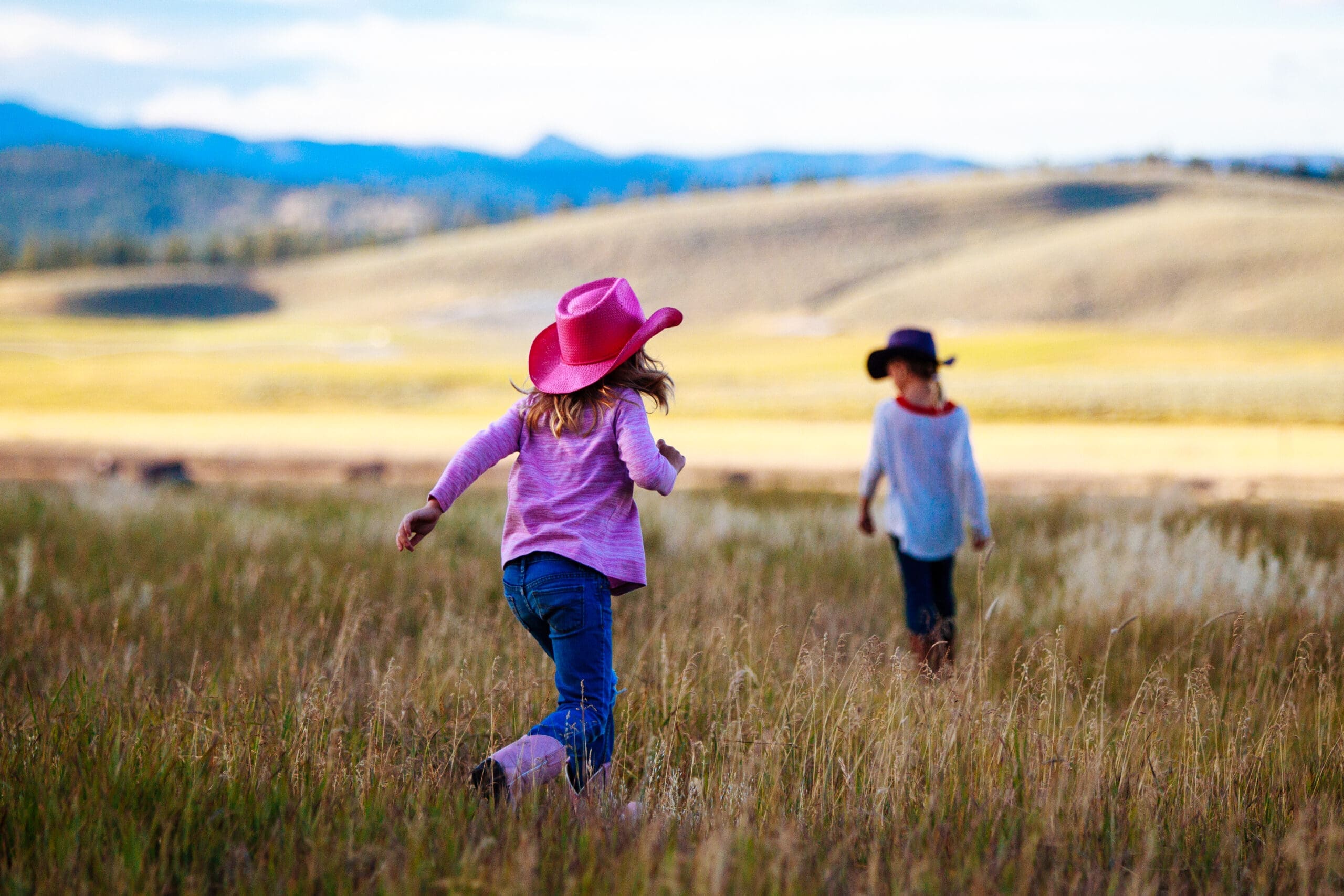 two little girls with cowgirl hats running in a field