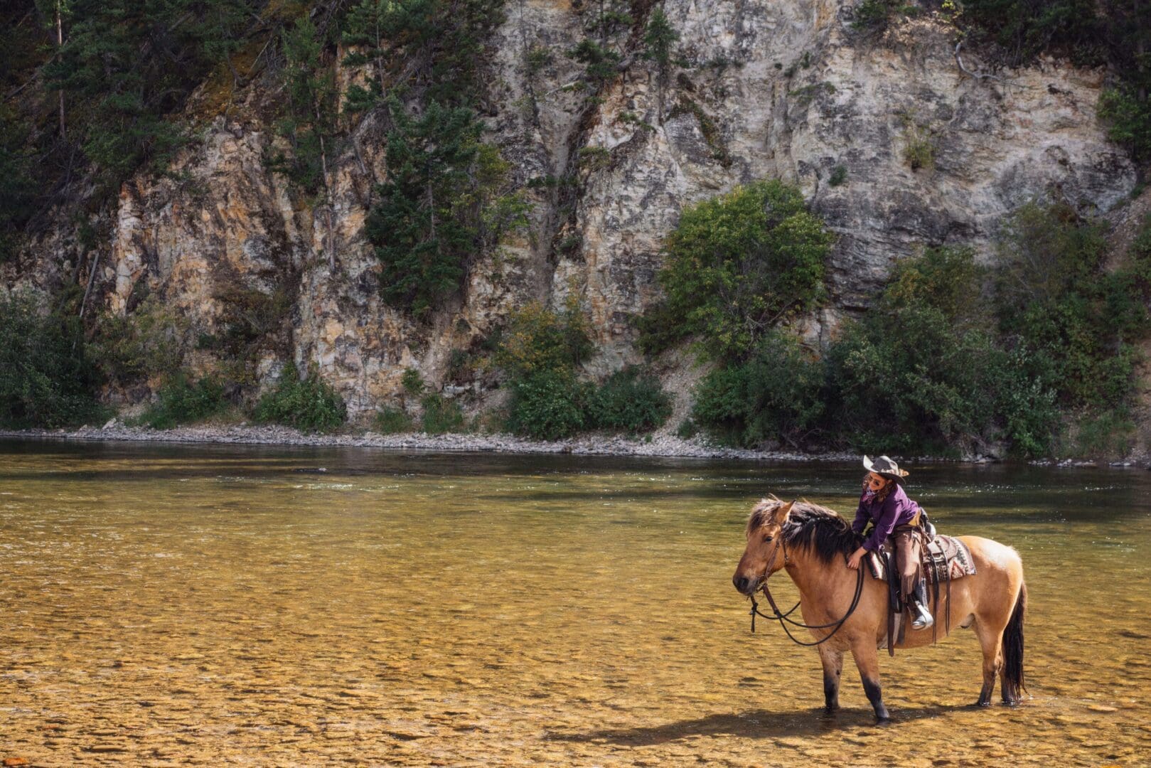 Lone cowgirl petting her horse while they are standing in a river.