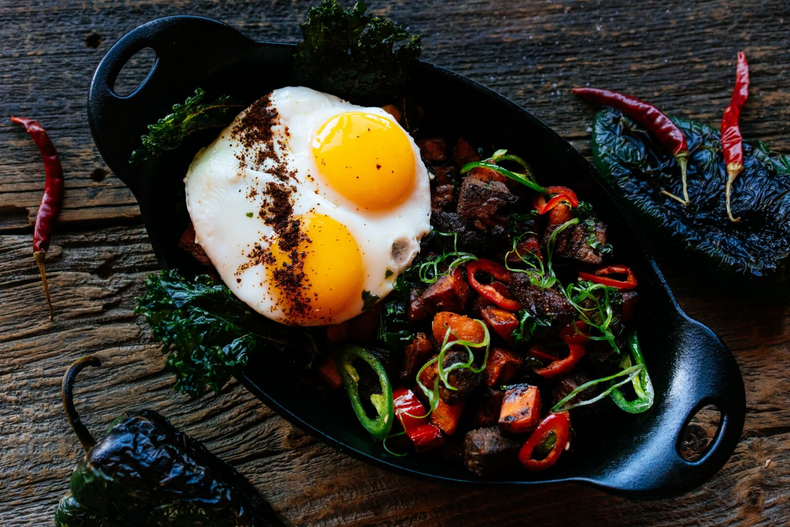Breakfast plate of eggs, steak, and peppers cooked in a cast iron dish.