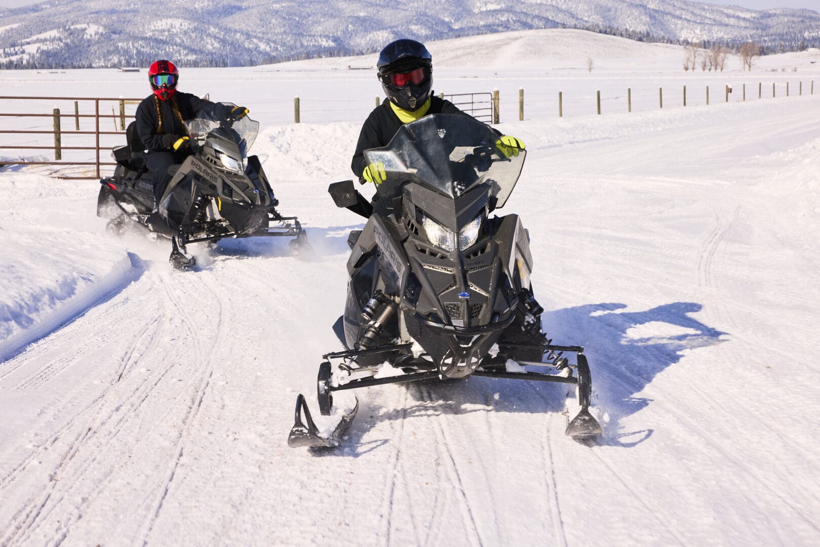 Two snowmobilers driving down a snowy path.