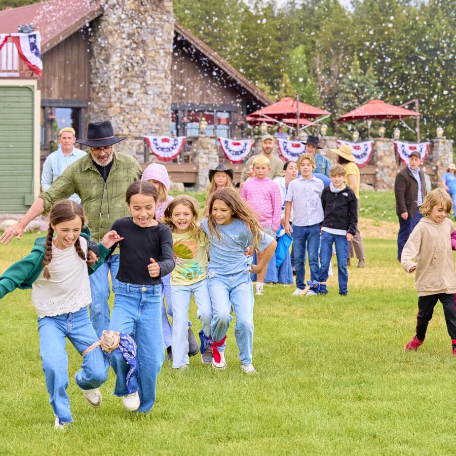 Children playing three-legged race on a grassy hill with fourth of July decorations behind them.