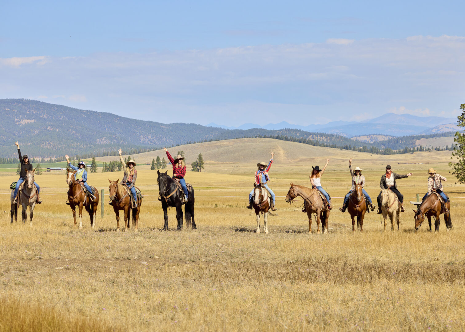 Group of cowgirls in a row, holding up their arms and cheering on horseback.