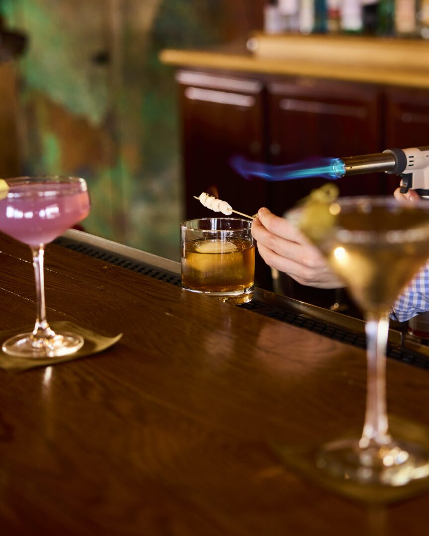 A bar counter with a person using a torch to flame a cocktail.