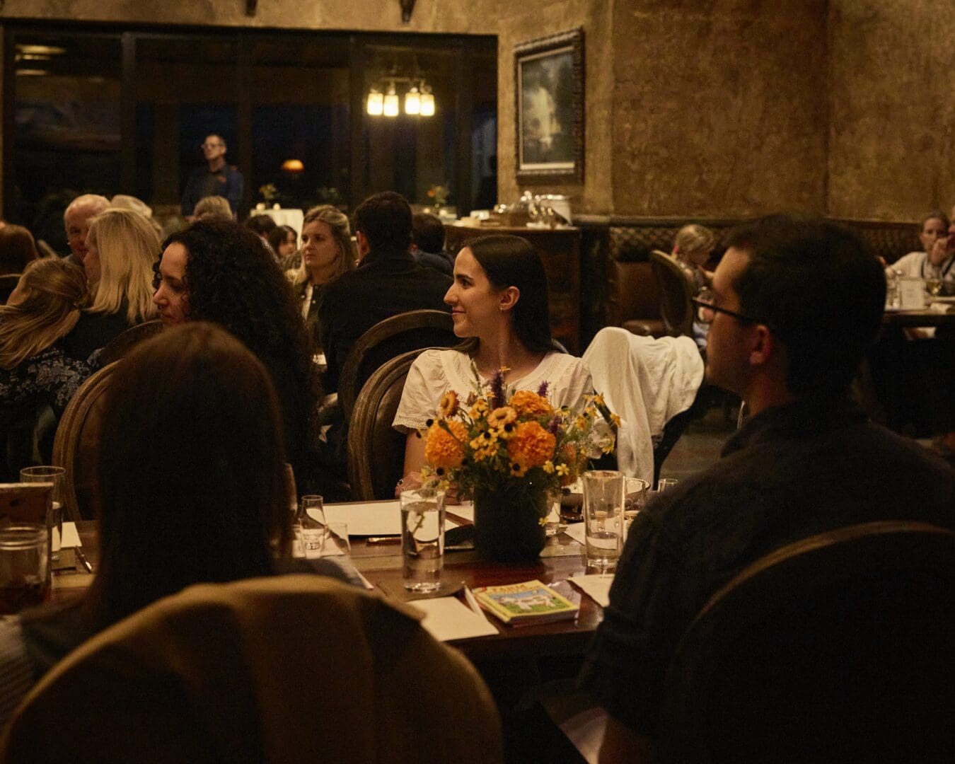 People in a dimly lit restaurant talking and smiling.