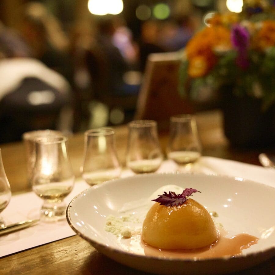 A dish set on a white plate with liquor tasting glasses in a row on the table.