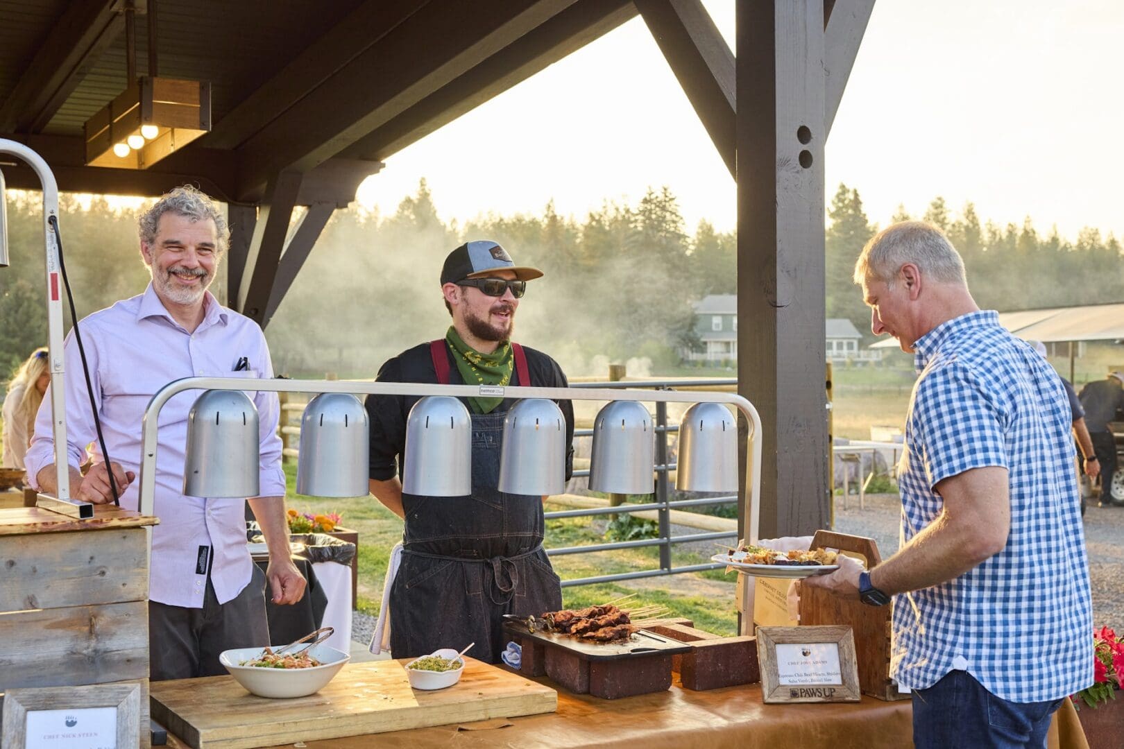 Chefs standing under a pavilion outside preparing dishes for guests.