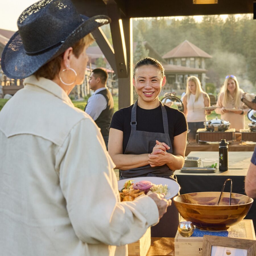 Chef clasping her hands in front of her as guests line up to get food from the buffet.