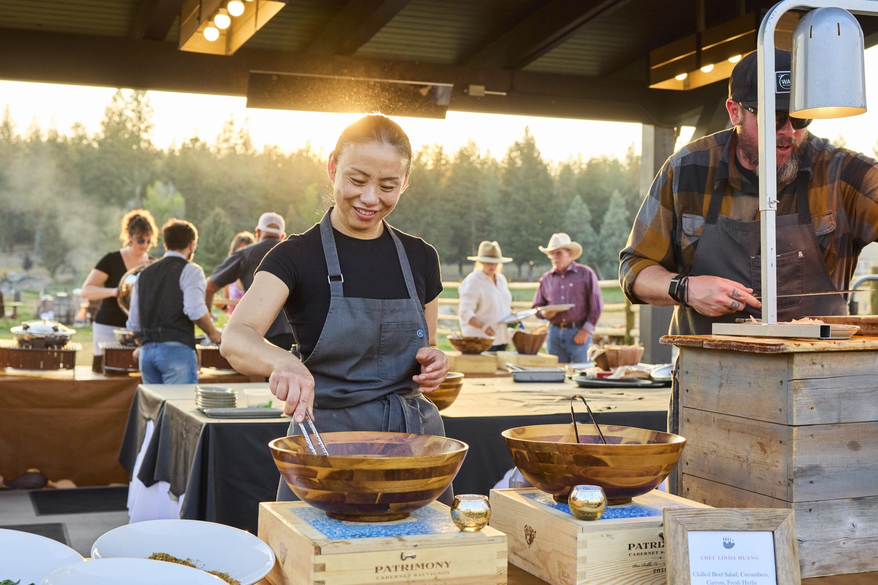 Chef standing under a pavilion outside preparing dishes for guests.