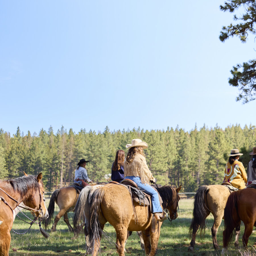 Group of cowgirls riding on a field with trees in front of them.