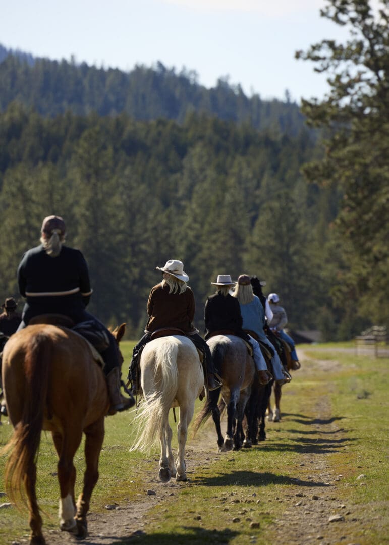 Group of cowgirls riding on a field with mountains in front of them.