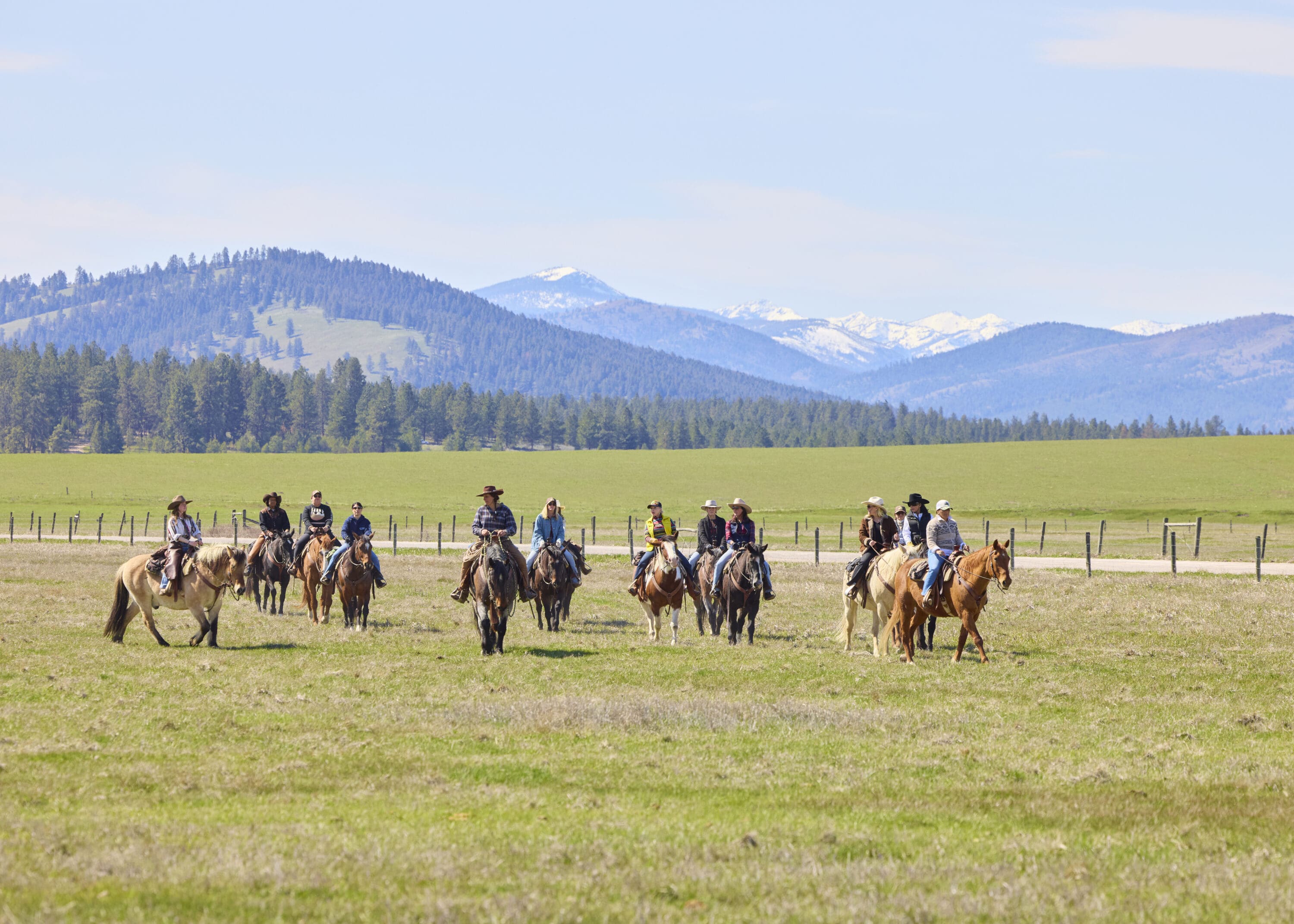 Group of cowgirls riding on a field with mountains behind them.