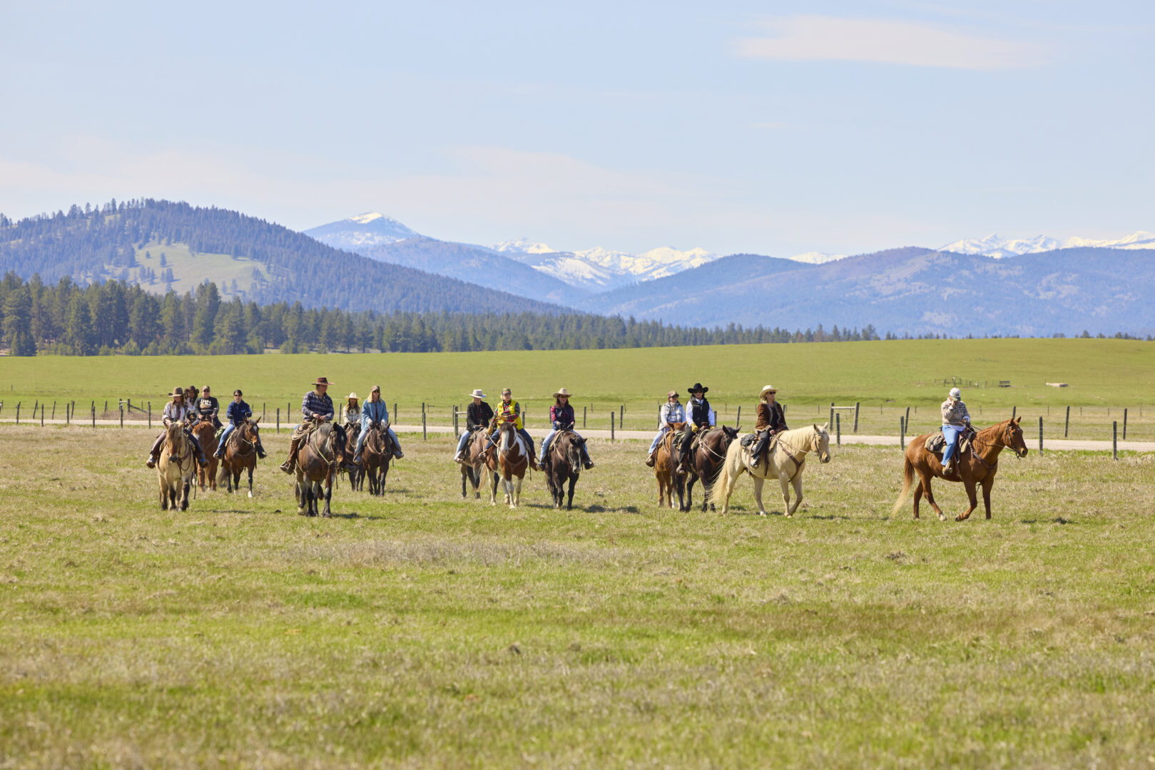 Group of cowgirls riding on a field with mountains behind them.