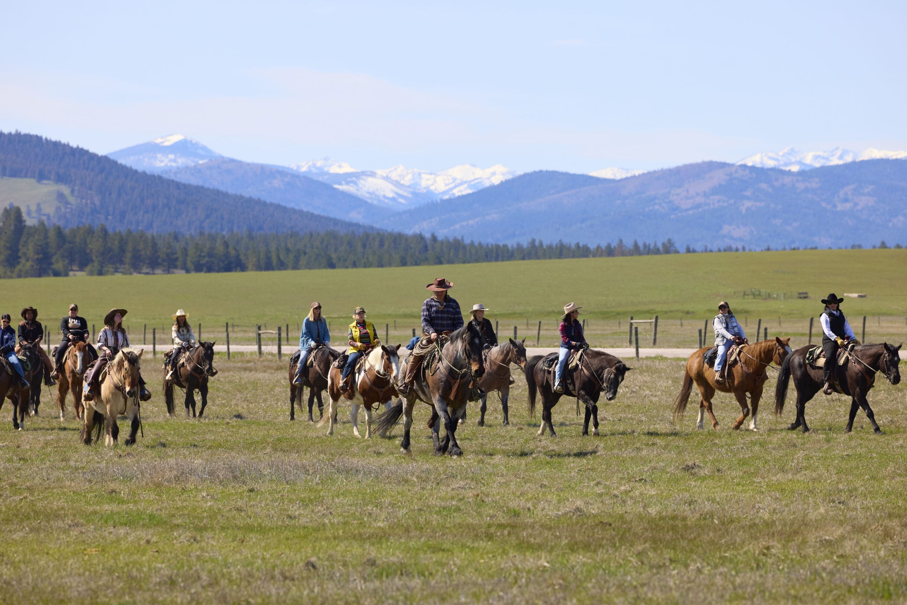 Group of cowgirls riding on a field with mountains behind them.