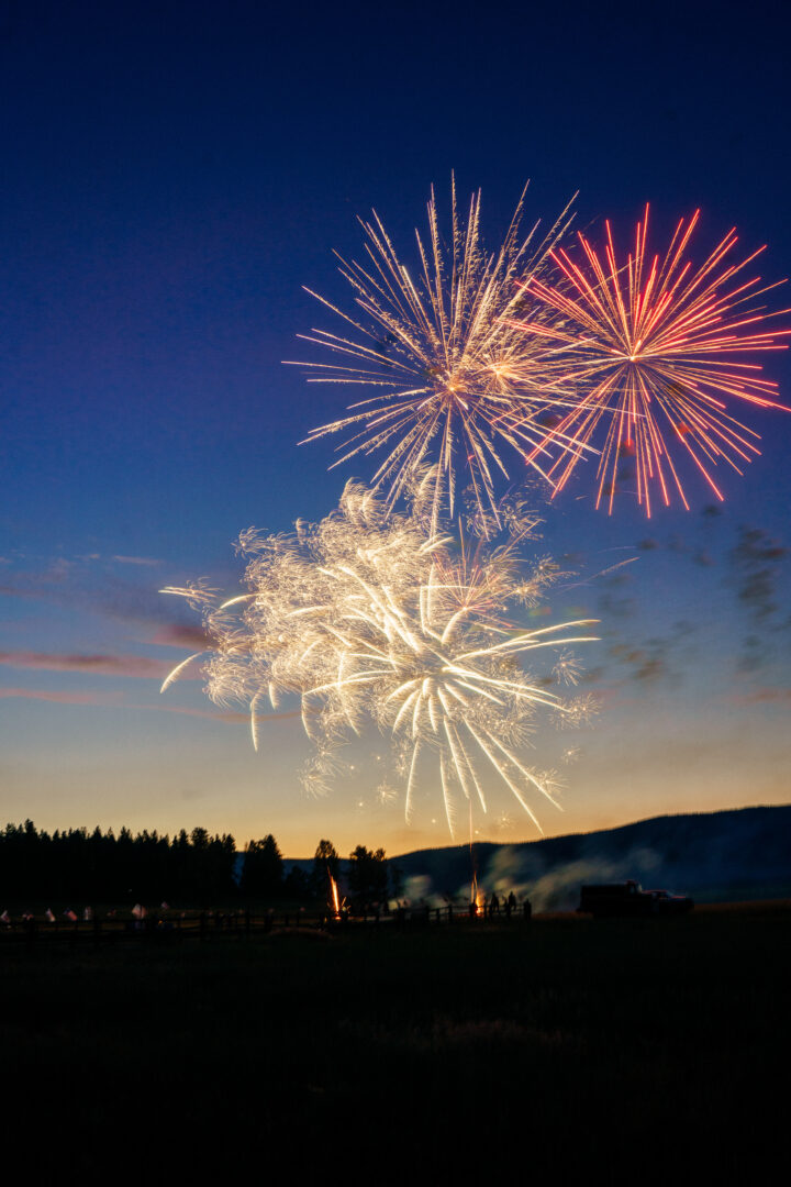 Red and white fireworks on a blue sky as the sun is setting.