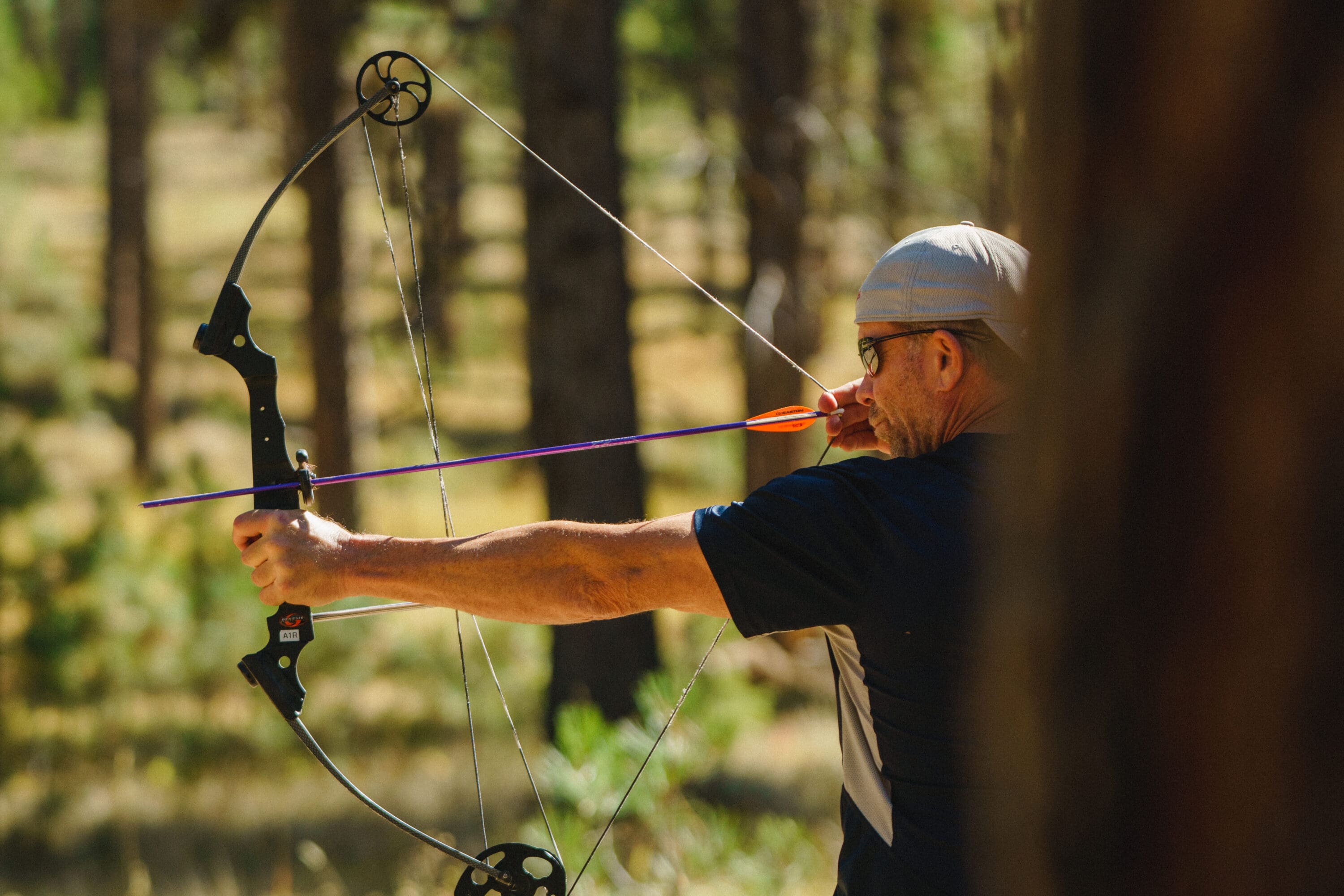 Man shooting a bow and arrow in a forest.