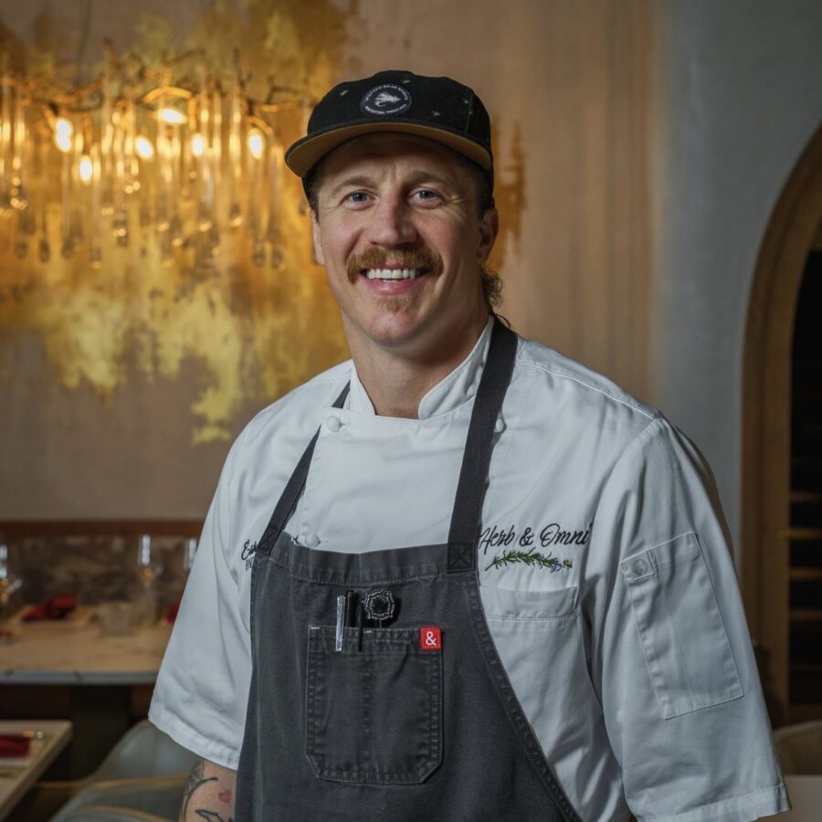 Chef wearing a black baseball cap and dark grey apron posing for a portrait photo.